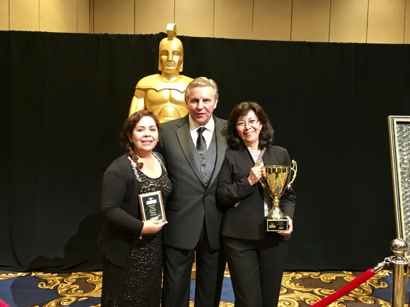 Patricia Moreno sonriente con su trofeo en una ceremonia de premiación, junto a dos colegas